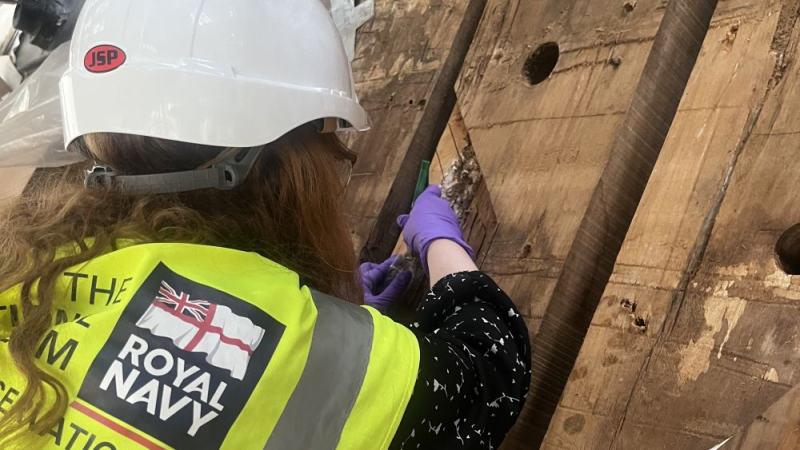 A conservator in high visibility gear inspects HMS Victory's wooden hull. 
