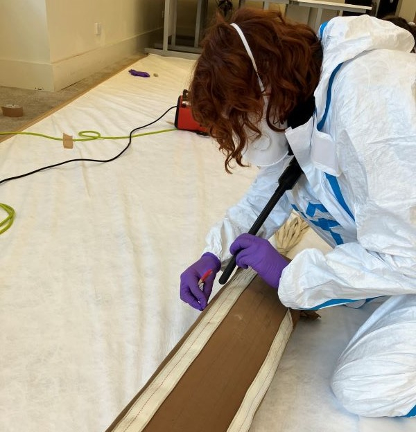 Allanah Hay in white protective gear doing conservation work on a plank. 