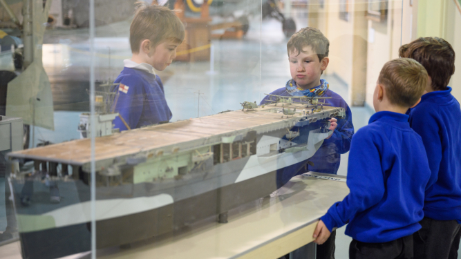 School children looking at a model of an aircraft carrier. 