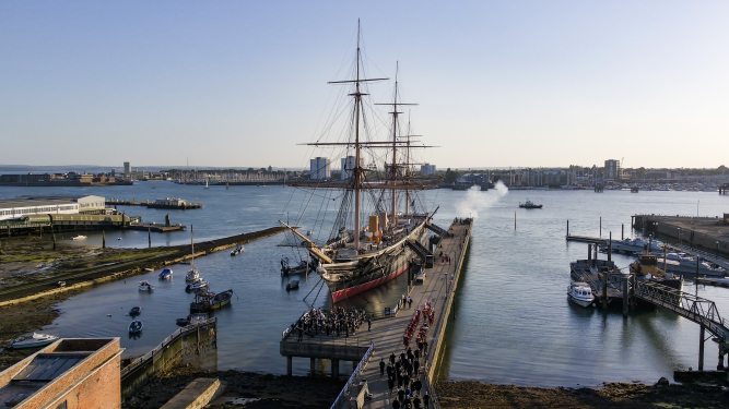 Drone shot of HMS Warrior at dock in Portsmouth Harbour surrounding by small civilian craft. 