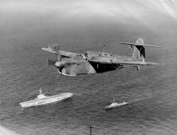A Fairey Barracuda flying over battle cruisers at sea. 
