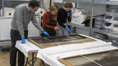 Three curators looking at a painting in the National Museum of the Royal Navy's collection. 