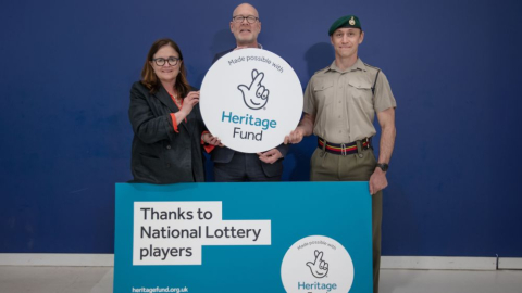 Matthew Sheldon holding the National Lottery Heritage logo with a Royal Marine. 