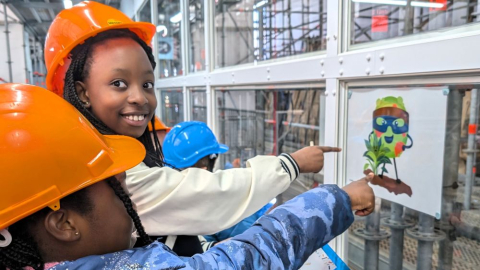 Children wearing hard hats point at a picture of fungi. 