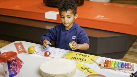 A child exploring shakers, a drum, and a xylophone at a 'Sounds of the Sea' sensory table