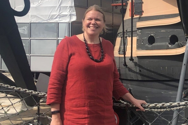 Lesley-Anne, a woman in red top, standing in front of HMS Victory.