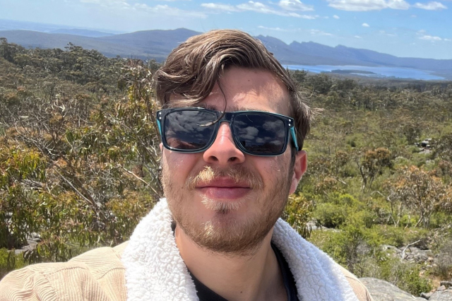 A young white man with brown hair and wearing sunglasses. 