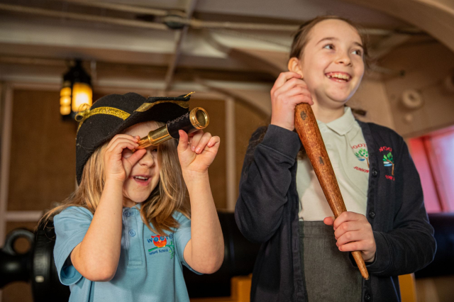 Two children holding replica ship tools onboard HMS Victory. 