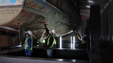 Conservators looking at the underside of a small boat.