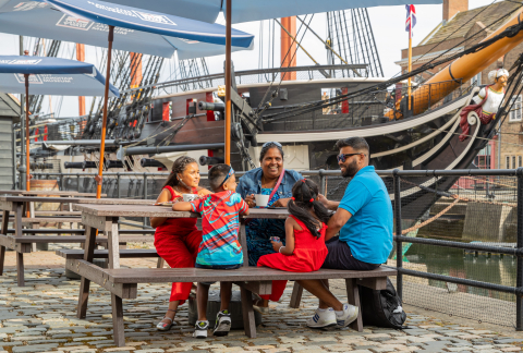 A family sitting on a bench in front of HMS Trincomalee.