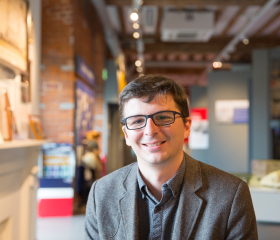 Andrew Baines smiles facing the camera with a museum gallery in the background.