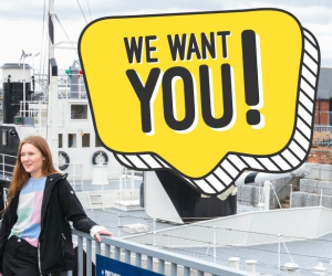 Two teenagers pose in front of HMS M.33 with a yellow speech bubble saying "We want you!".