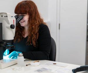 conservator looking at coins through a microscope