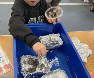 A child holding a pot of stones over a tray of water during 'Little Steamers: Float My Boat'
