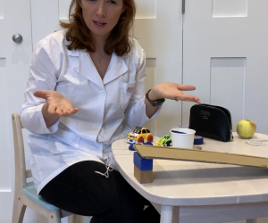 Presenter in a lab coat and safety goggles demonstrating a ramp experiment with toy cars for 'Little Steamers: Marvellous Machines'