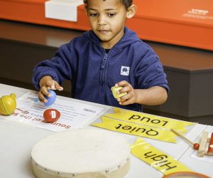 A child exploring shakers, a drum, and a xylophone at a 'Sounds of the Sea' sensory table
