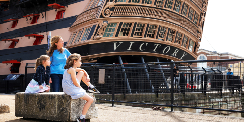 Family sitting in front of HMS Victory's stern at Portsmouth Historic Dockyard.