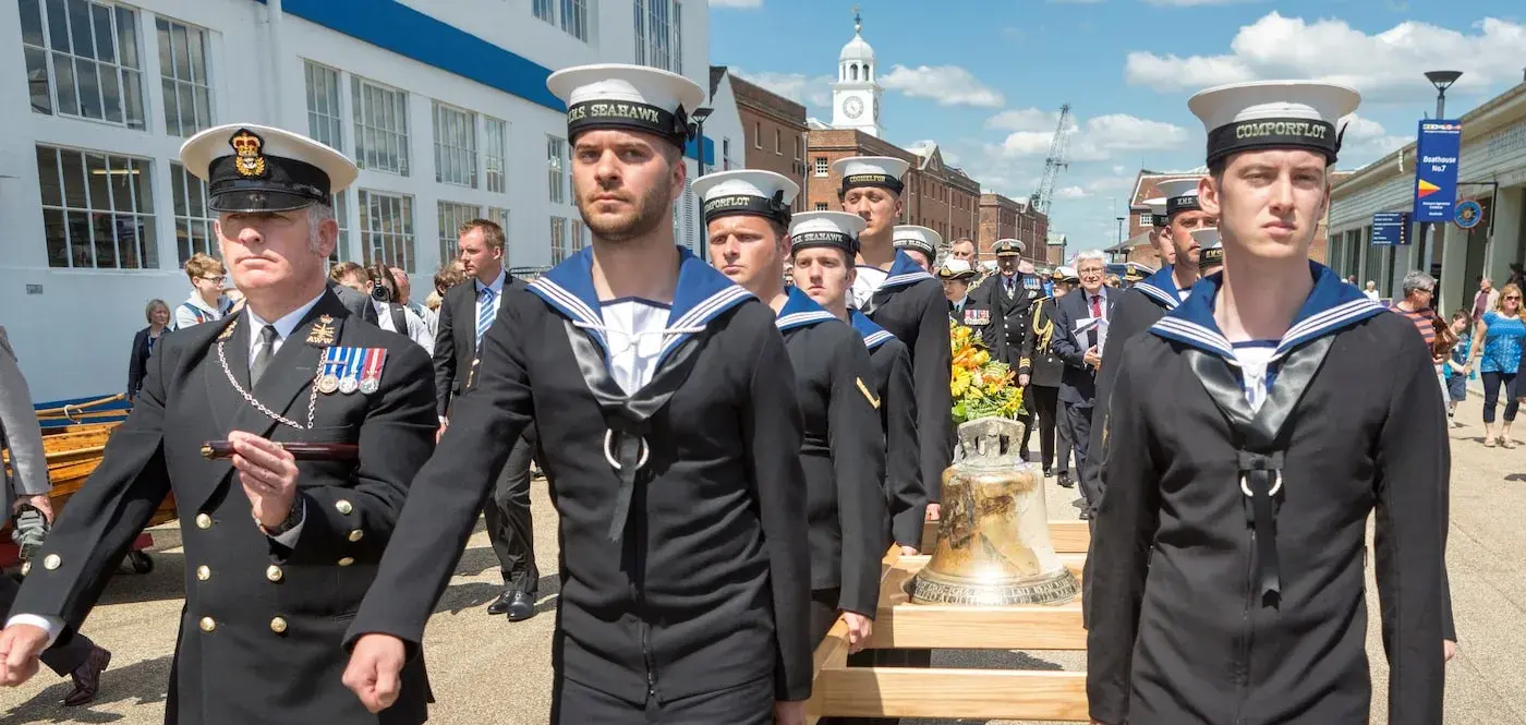 Royal naval personnel solemnly carrying the bell of HMS Hood through Portsmouth Historic Dockyard.  