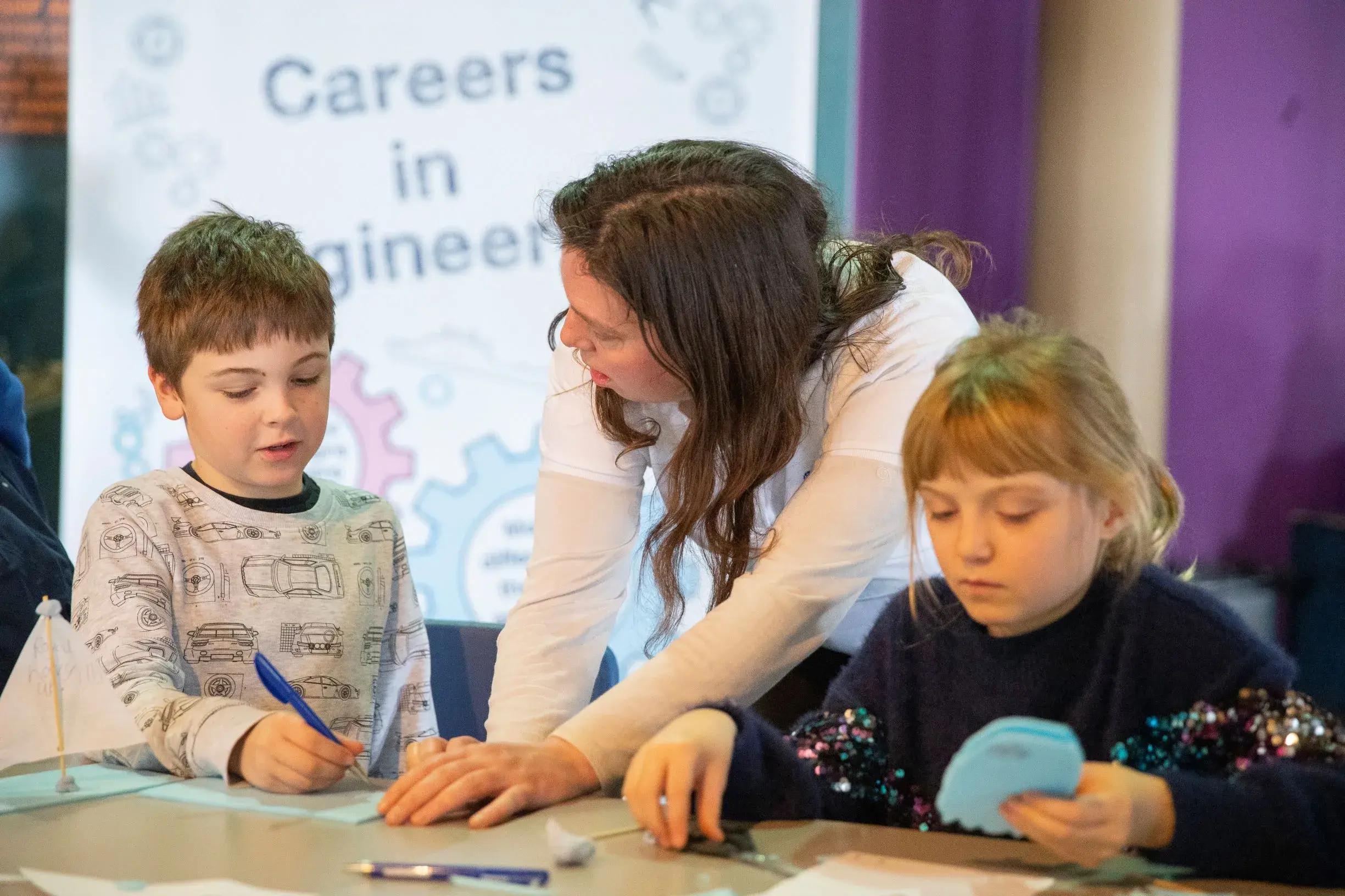 A woman and two children sit at a table engaging in a STEM activity.