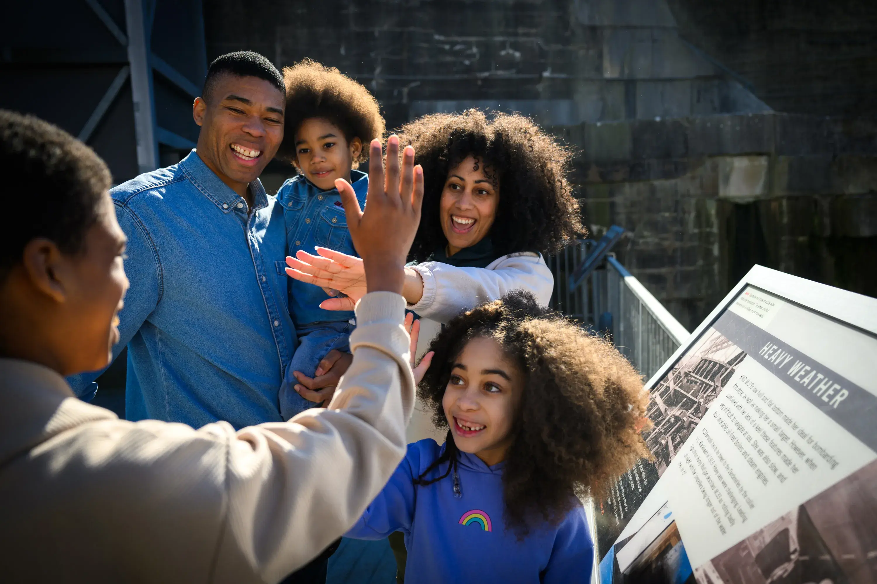Family laughing and high-fiving beside an information panel at HMS M33